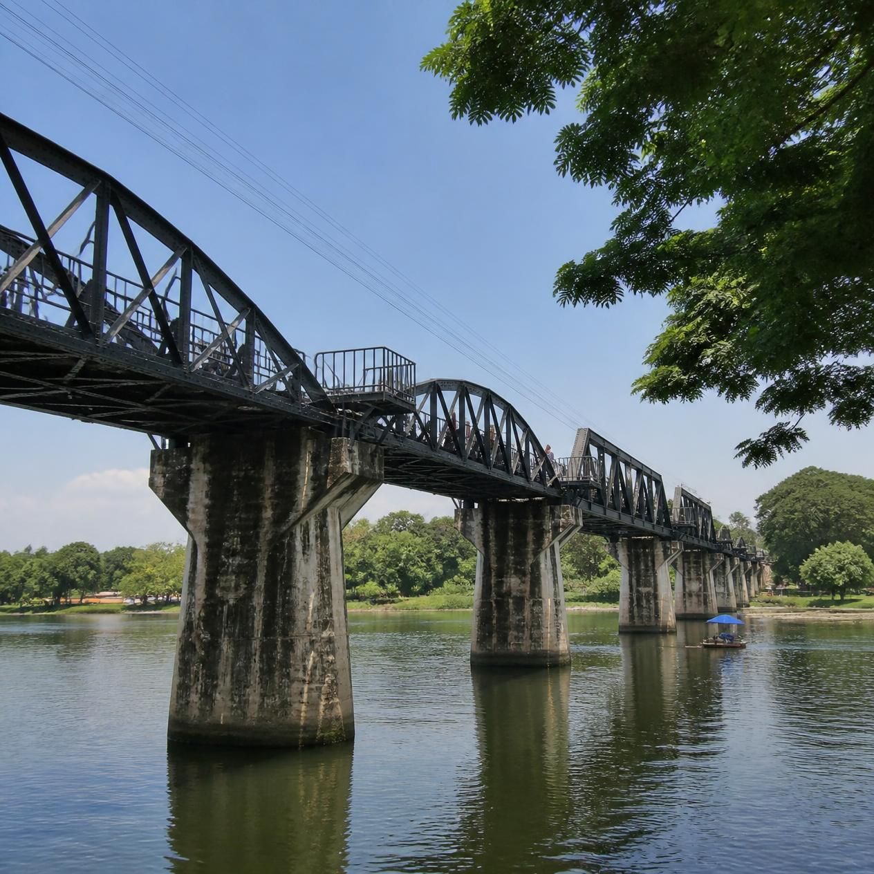 Black steel spans of the Bridge over the River Kwai crossing the river at Kanchanaburi on a day trip from Bangkok