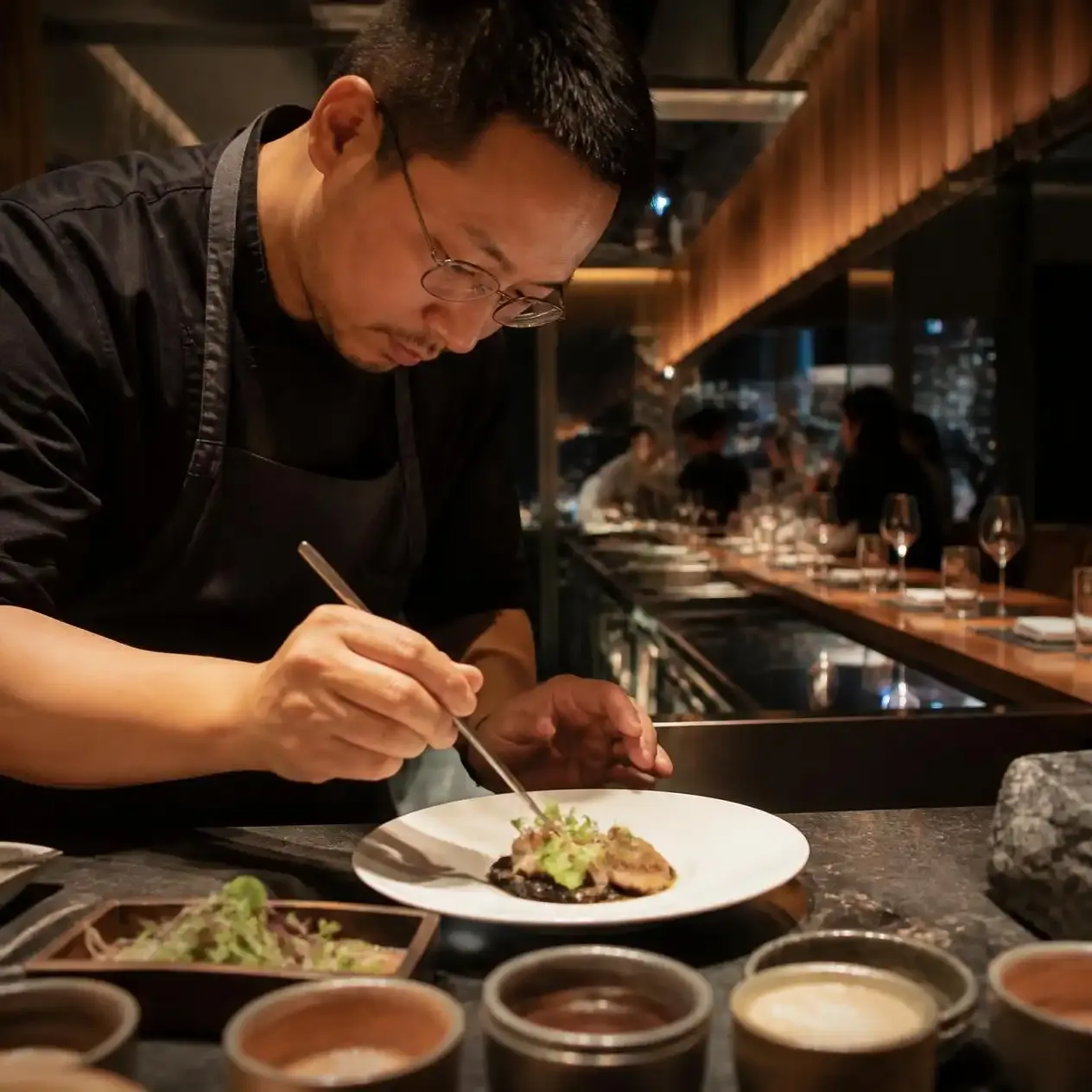 Chef plating a course at the open kitchen counter of a fine dining restaurant in Bangkok