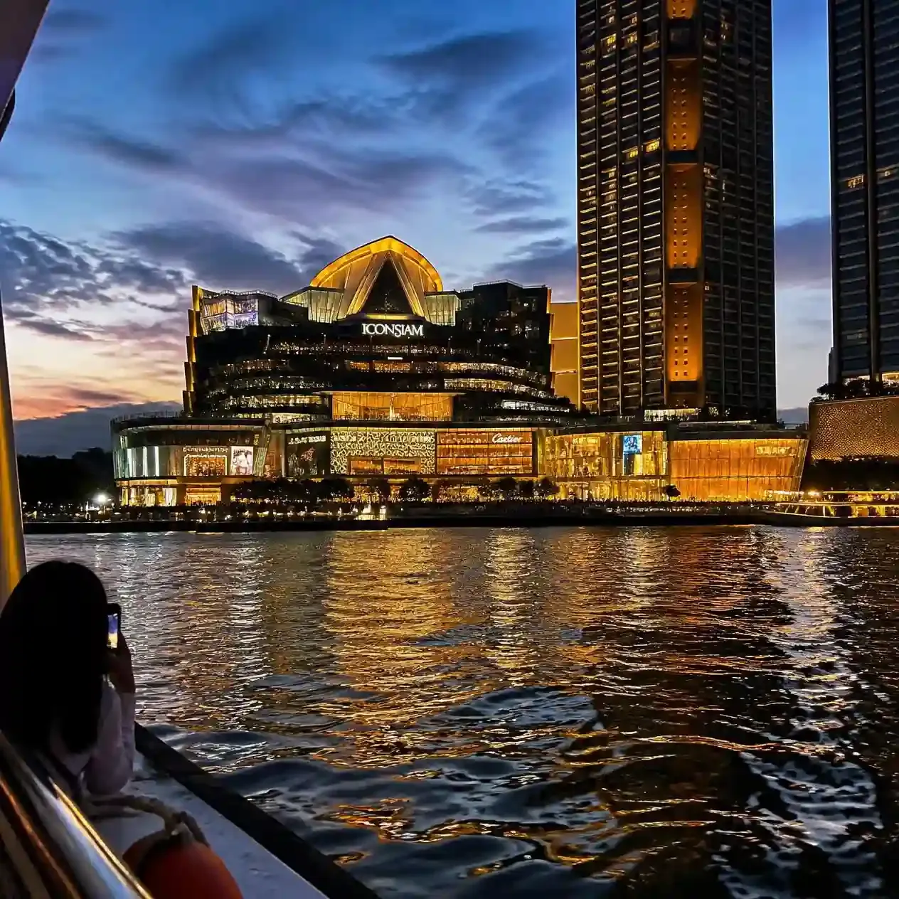 The illuminated glass frontage of ICONSIAM Bangkok seen from the Chao Phraya River at dusk