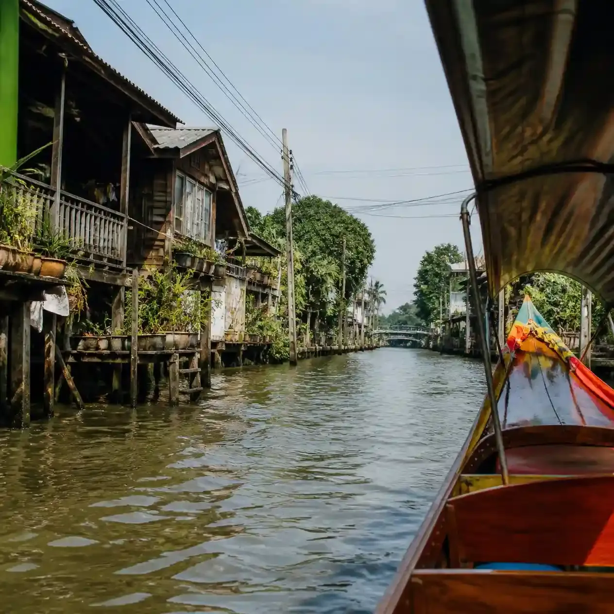 Long-tail boat passing wooden stilt houses along a Thonburi canal on a Bangkok food and canal tour