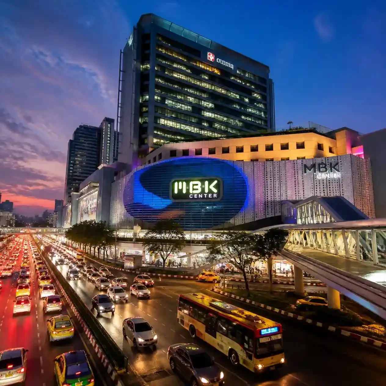 MBK Center Bangkok lit up at dusk viewed from the elevated Siam skywalk in Pathum Wan