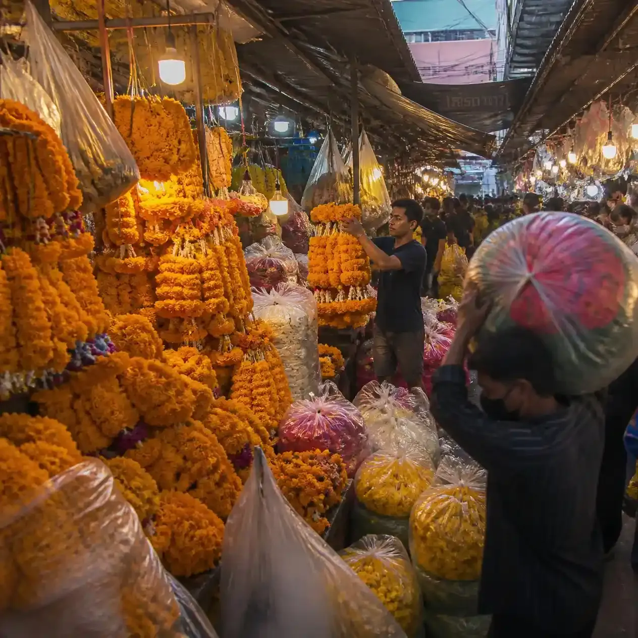Vendor lifting a bundle of marigold garlands in the pre-dawn aisles of Pak Khlong Talat flower market in Bangkok
