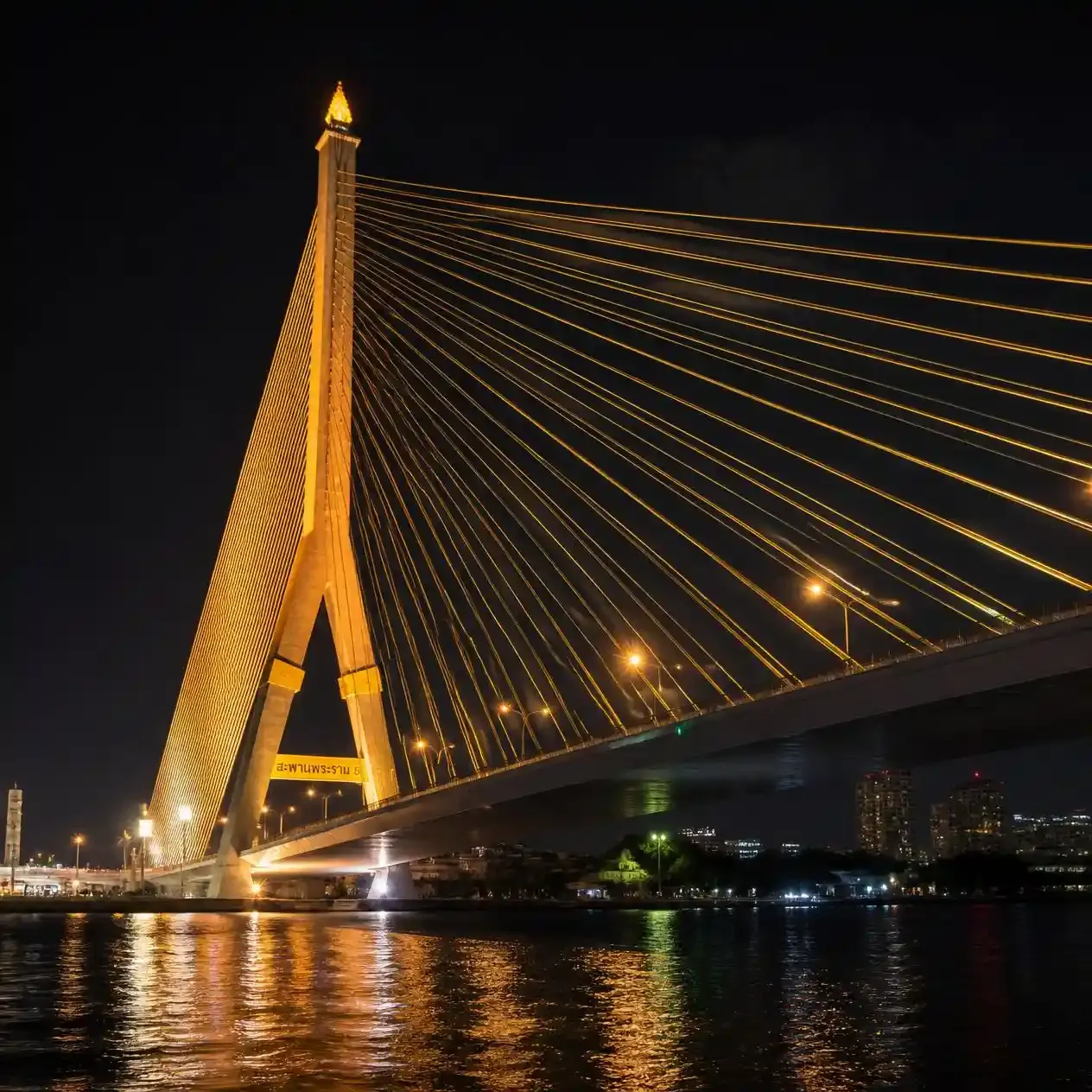 The cable-stayed Rama VIII Bridge illuminated at night seen from river level on the Chao Phraya in Bangkok