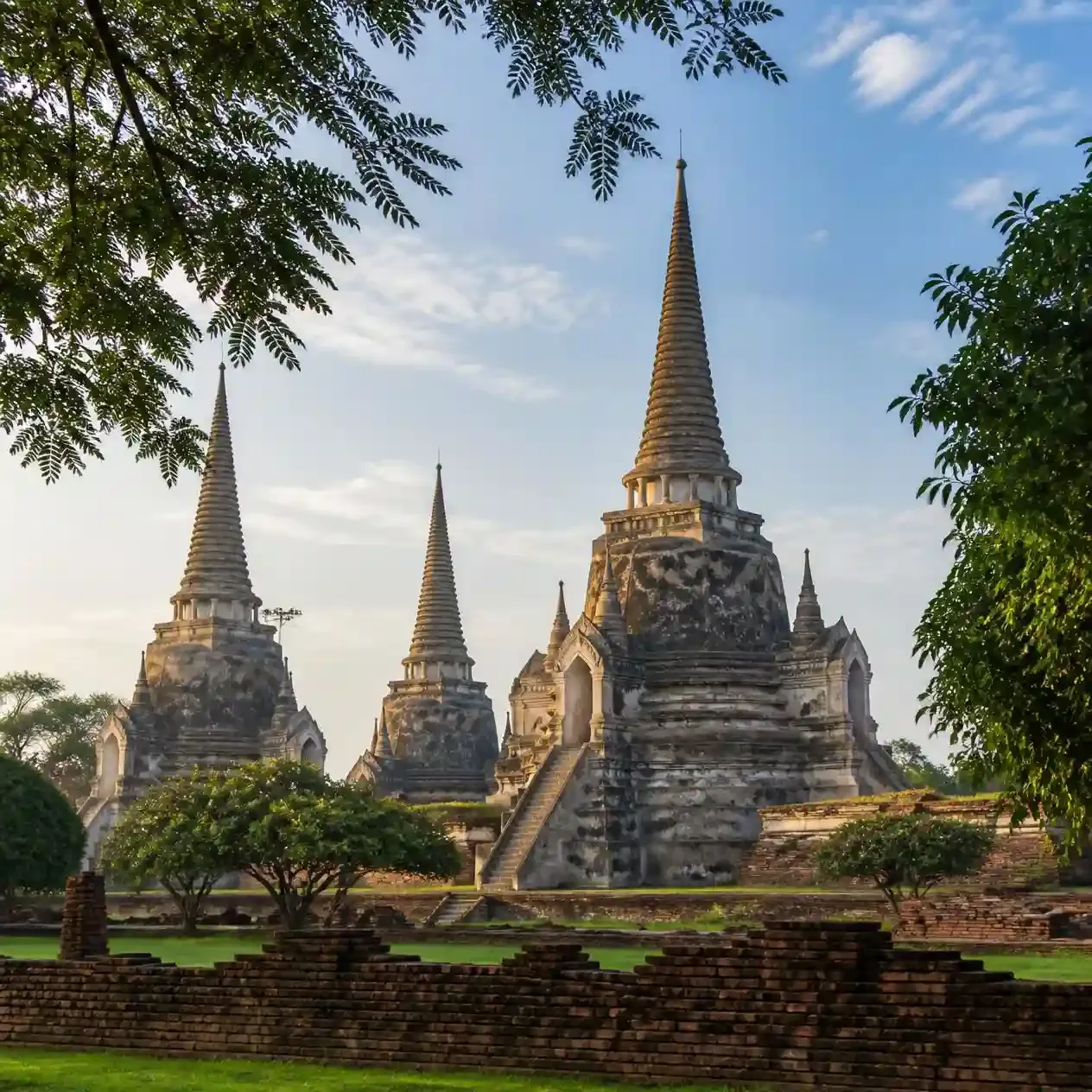Three restored bell-shaped chedis of Wat Phra Si Sanphet standing in a row under morning light at Ayutthaya Historical Park
