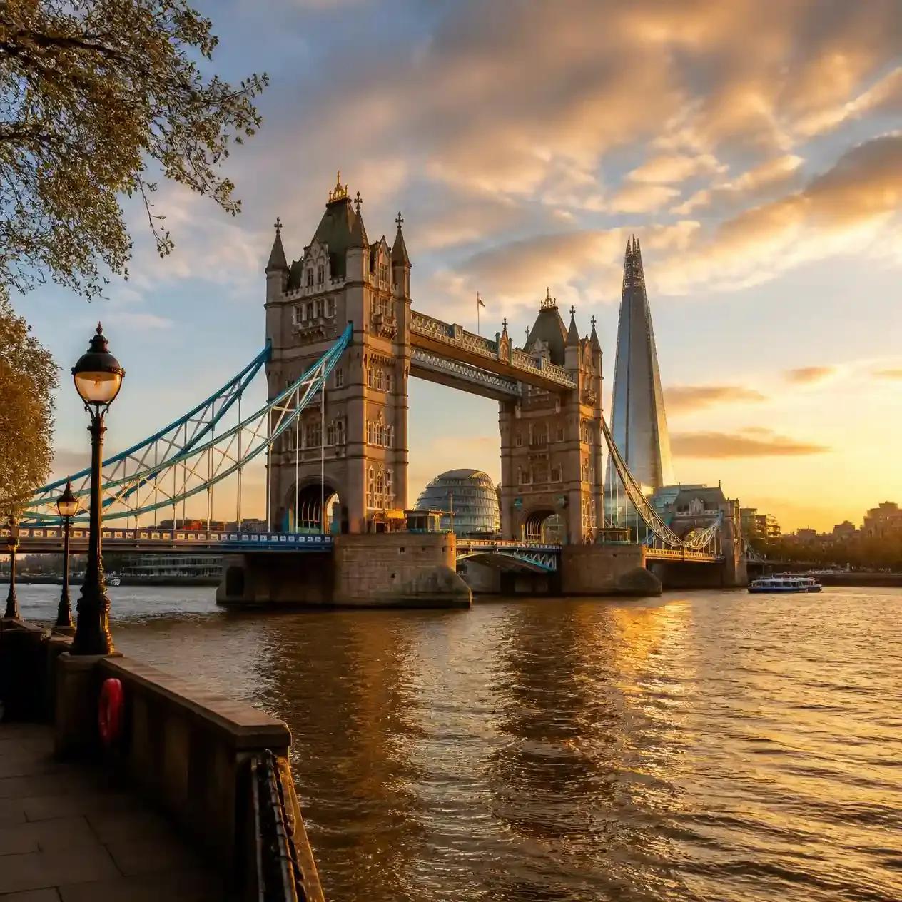 Tower Bridge lit by golden hour light over the River Thames with The Shard behind, seen from the north bank in London