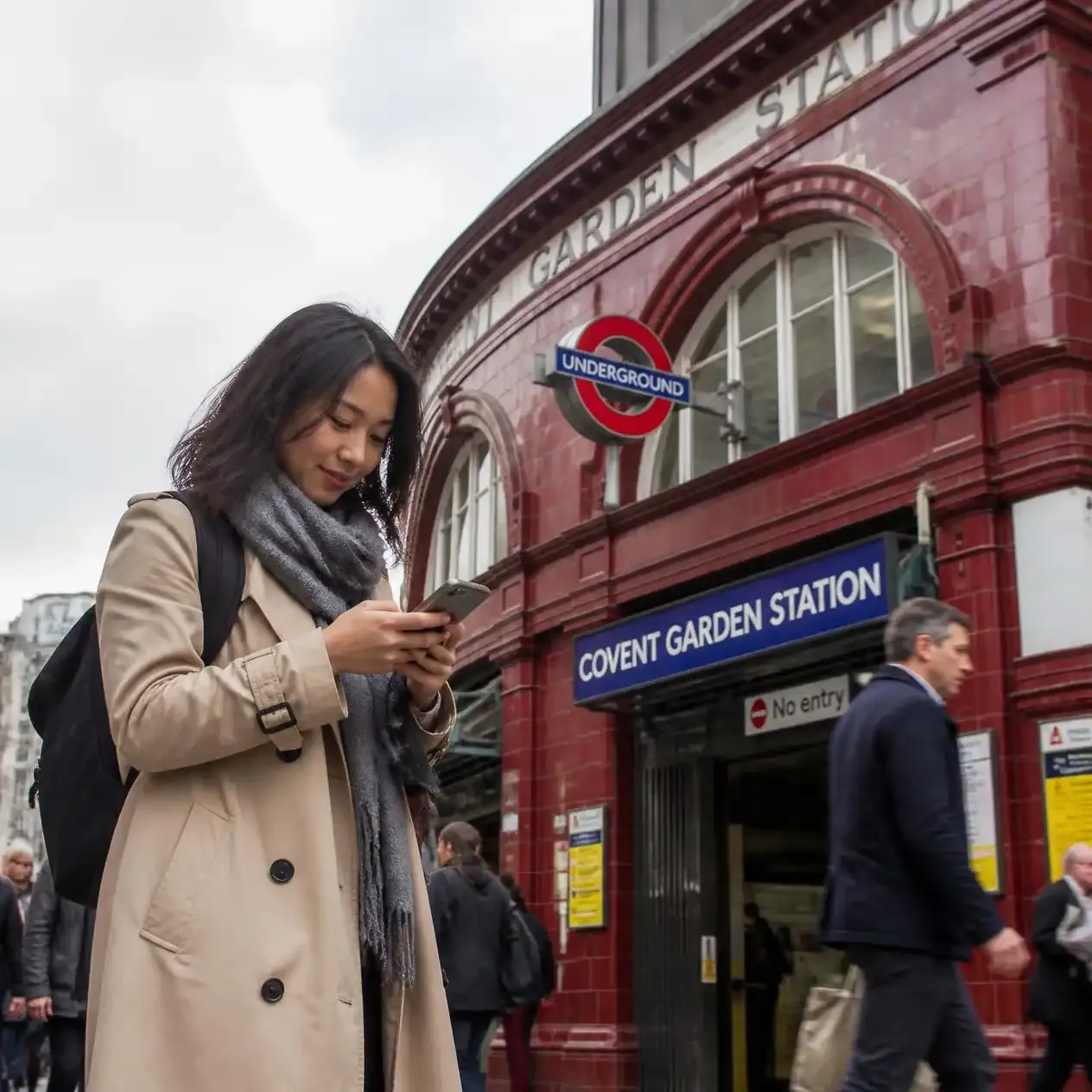 Tourist checking a navigation app on a phone outside a London Underground station entrance