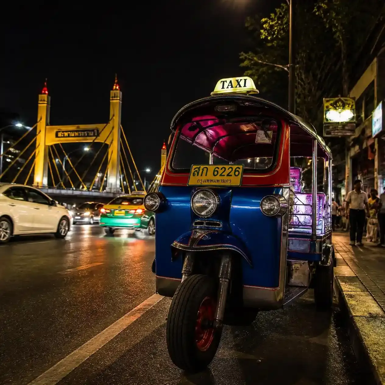 Tuk-tuk parked on Chak Phet Road at night outside the Bangkok flower market with Memorial Bridge lit behind