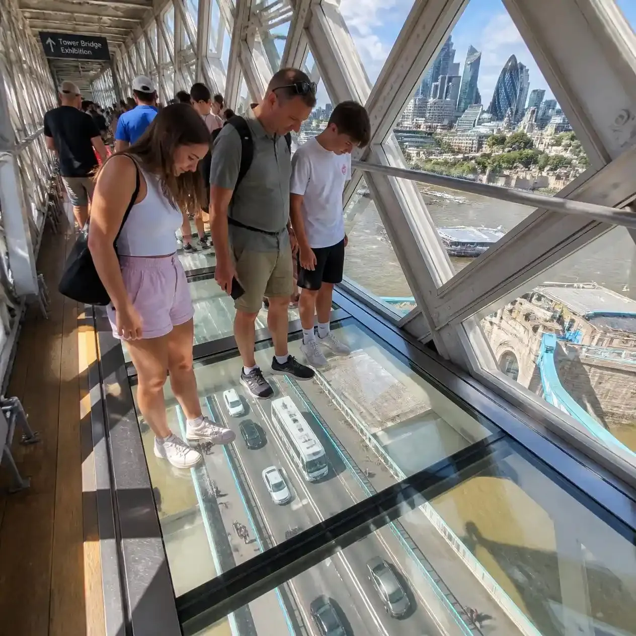 Visitors on the Tower Bridge Exhibition glass floor walkway watching buses and traffic pass 42 metres below on the bridge
