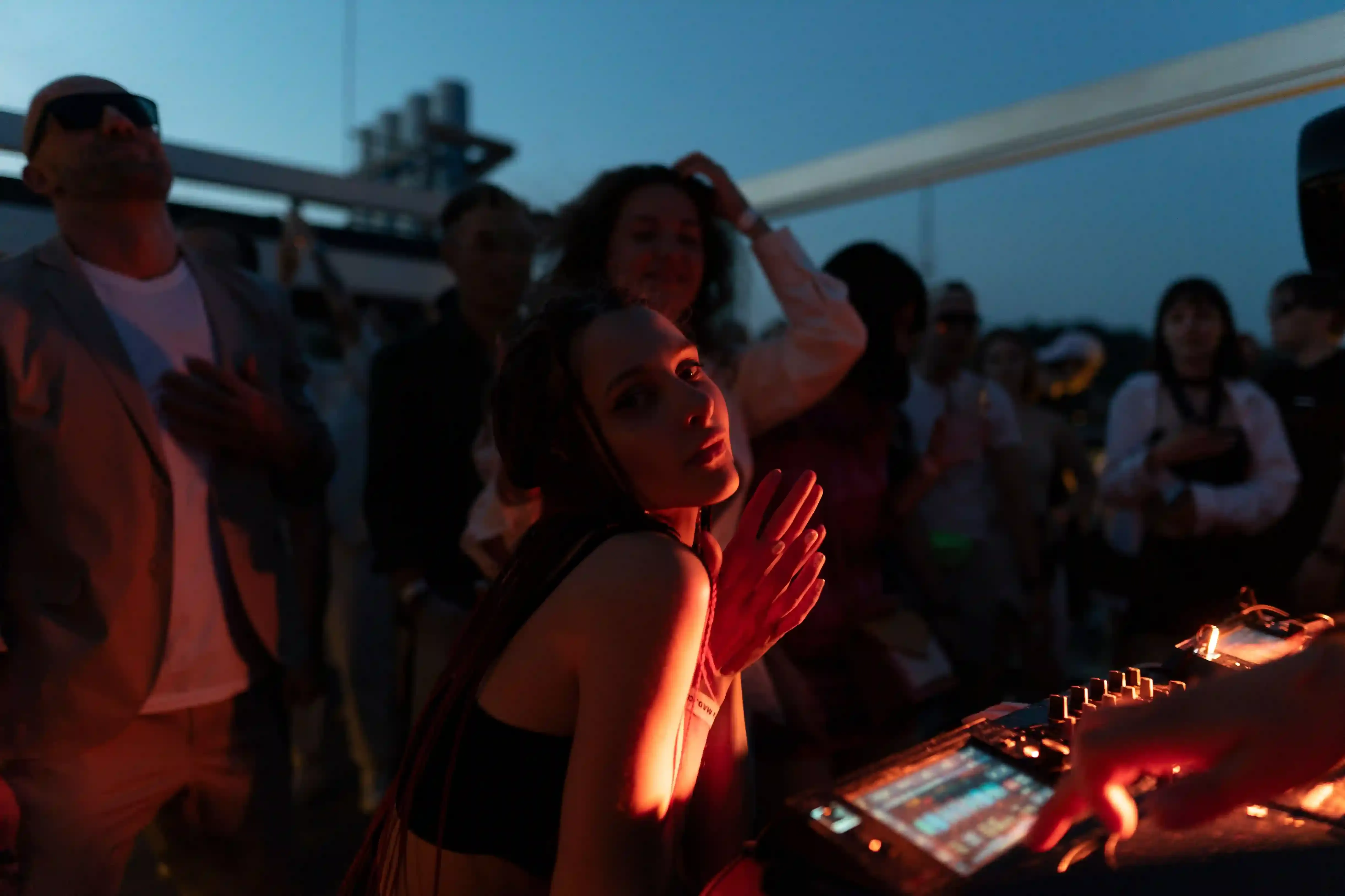 A DJ and crowd dancing on the open top deck of a Thames party boat at night with the lit London skyline behind