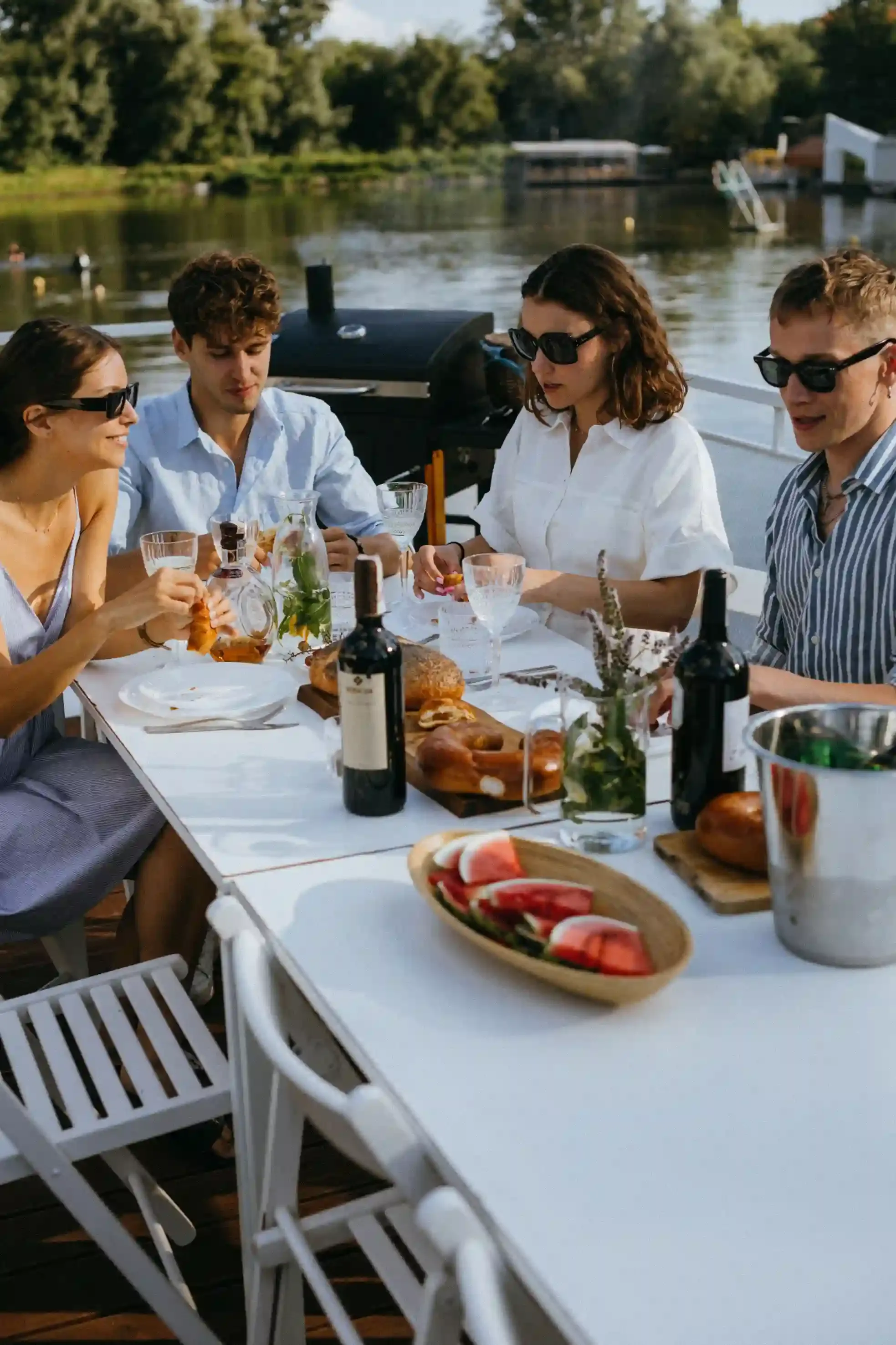 A group celebrating at a bottomless brunch party cruise table on the Thames with prosecco and the London skyline behind