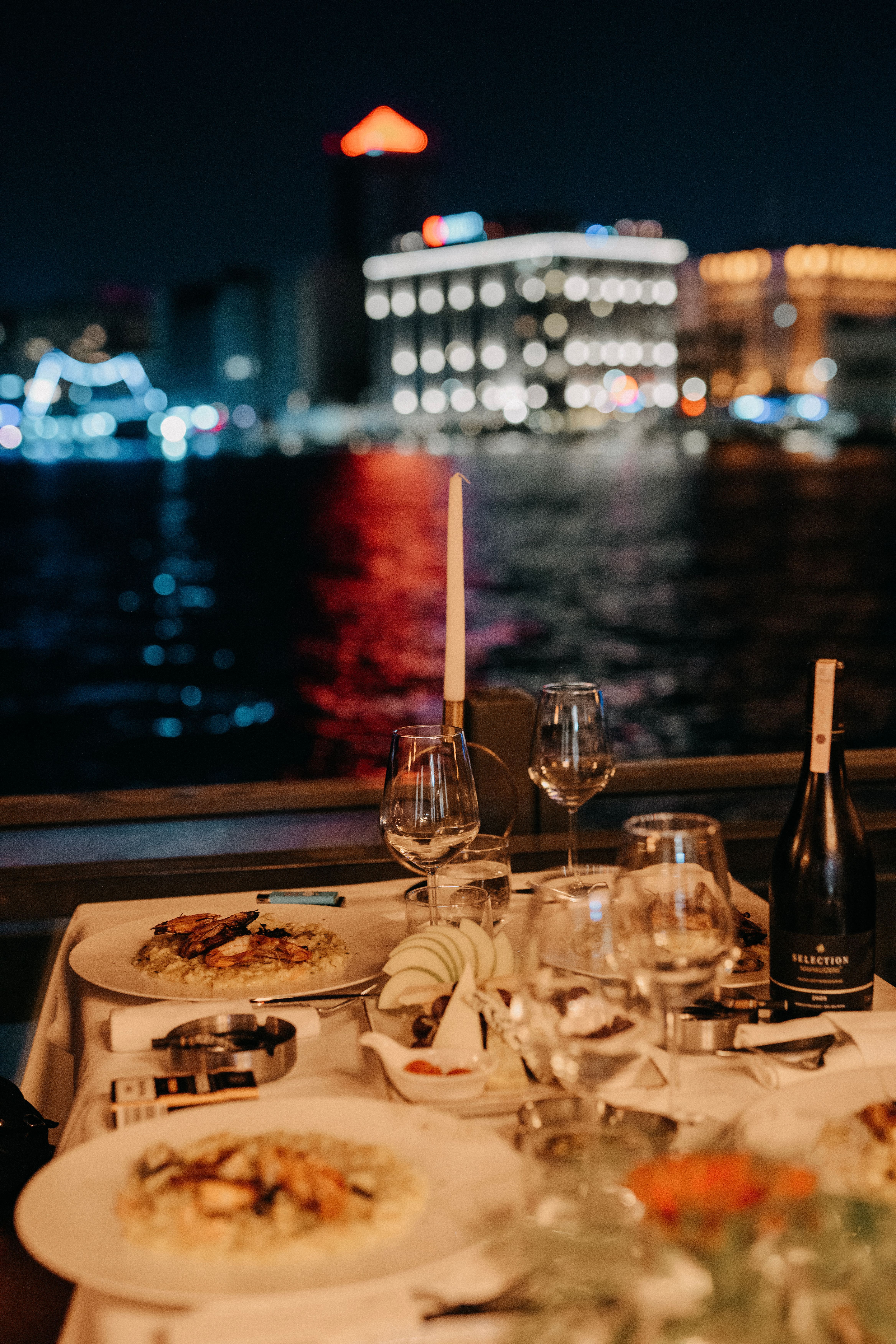 A dinner cruise table set against the illuminated London skyline at night on a Thames river cruise