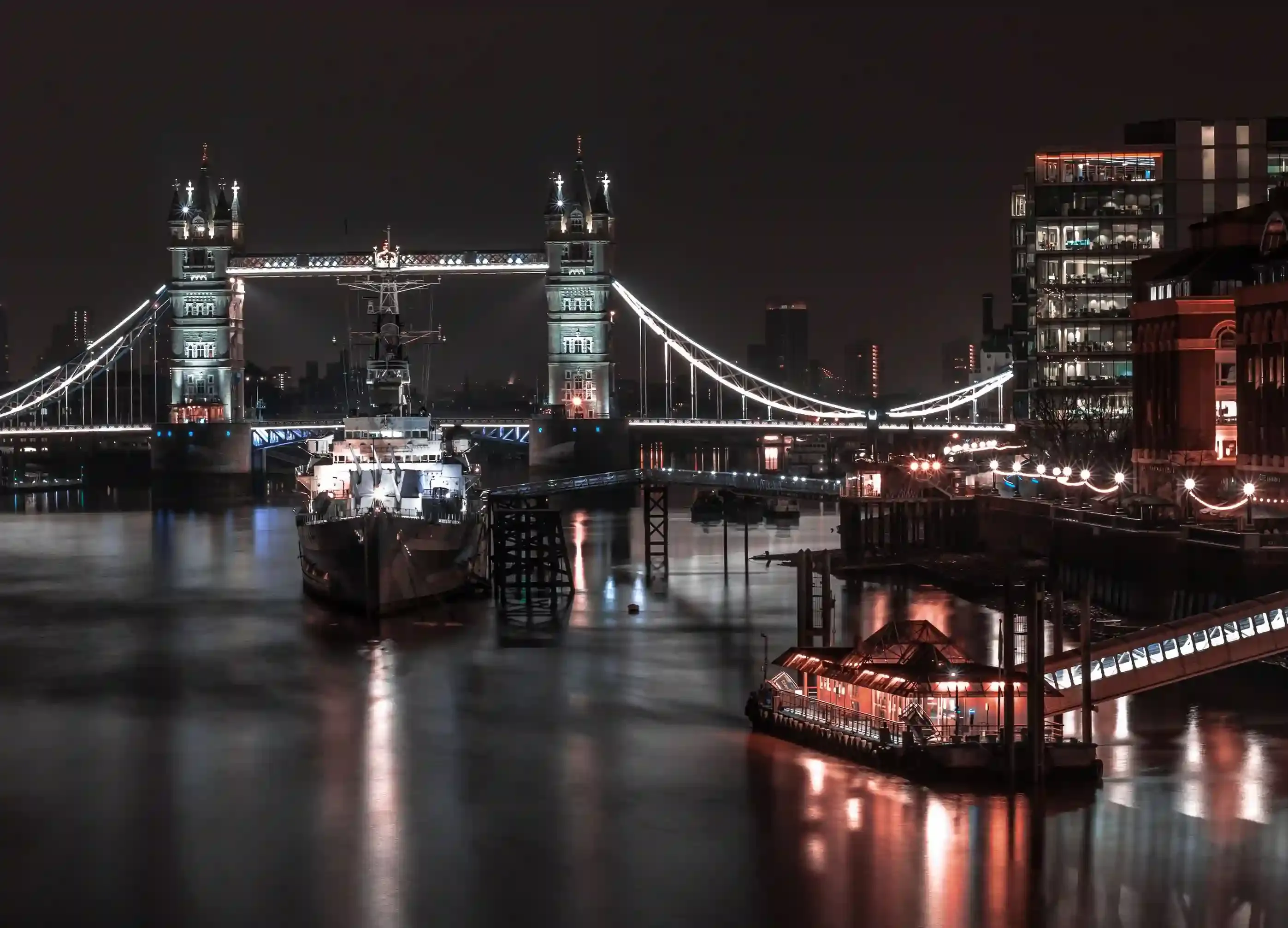 A lit-up party boat cruising on the River Thames at night with Tower Bridge illuminated in the background in London