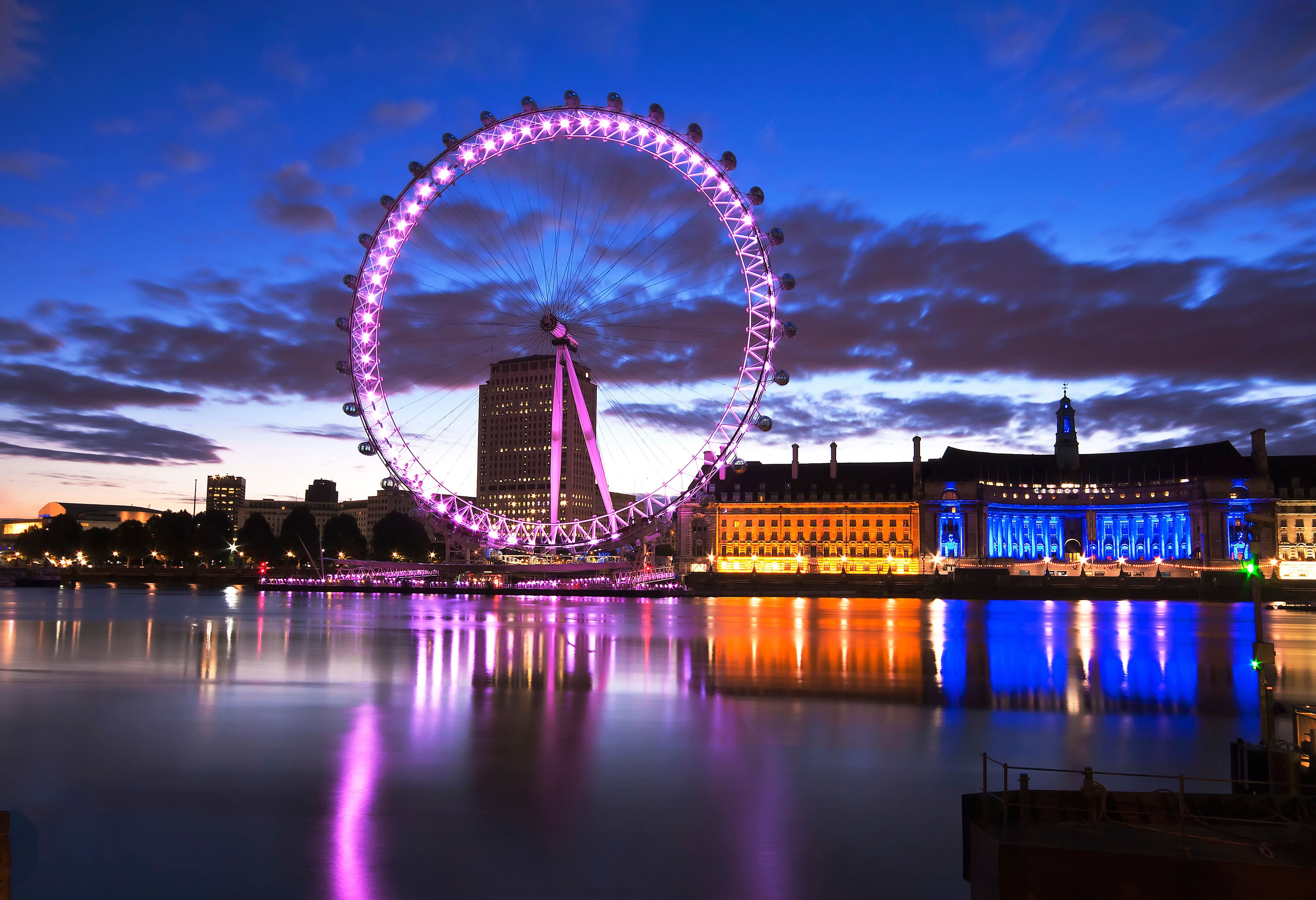 The illuminated London Eye and County Hall on the South Bank of the River Thames at dusk in London