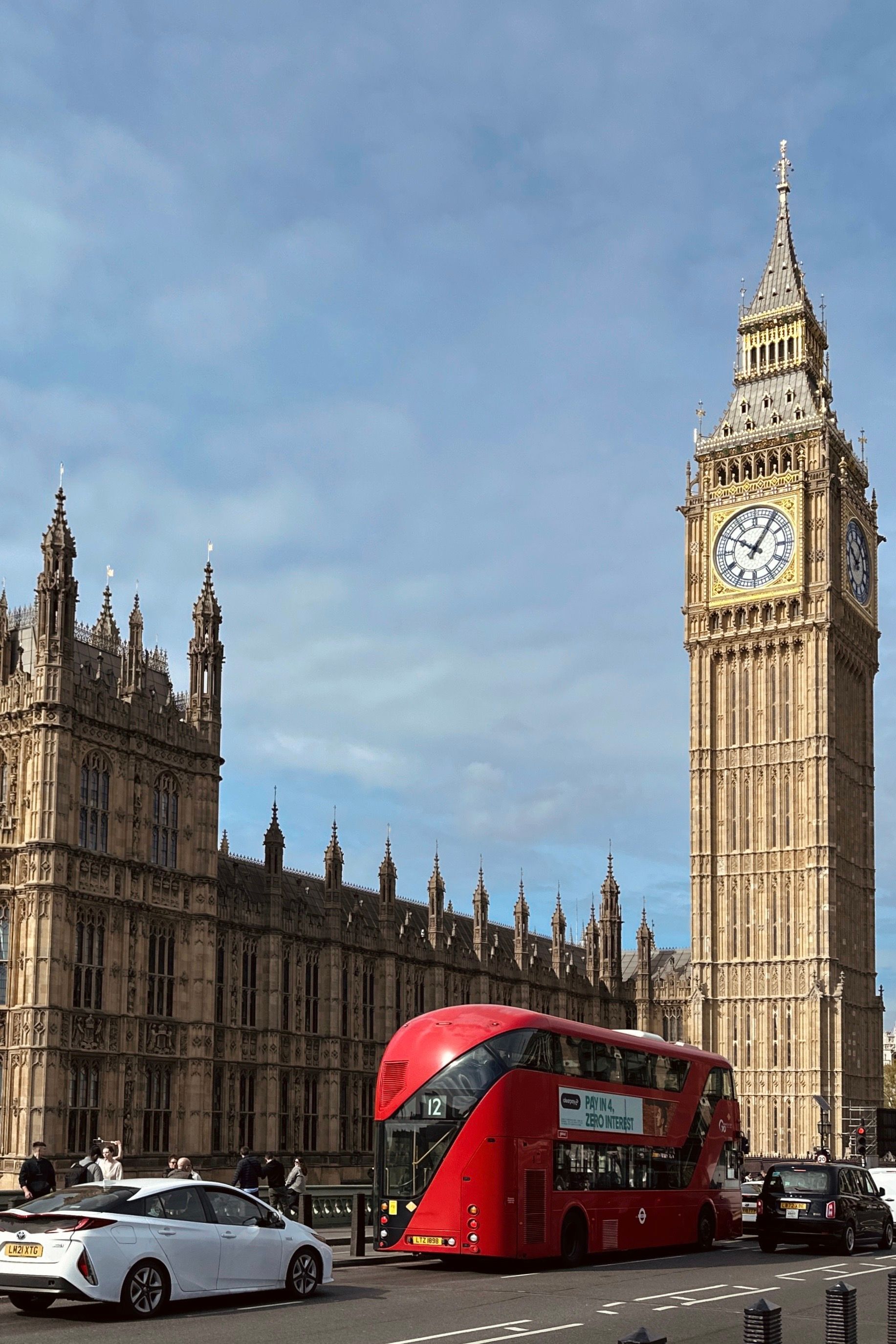 Open-top red double-decker London sightseeing bus passing Big Ben and the Houses of Parliament on a clear day