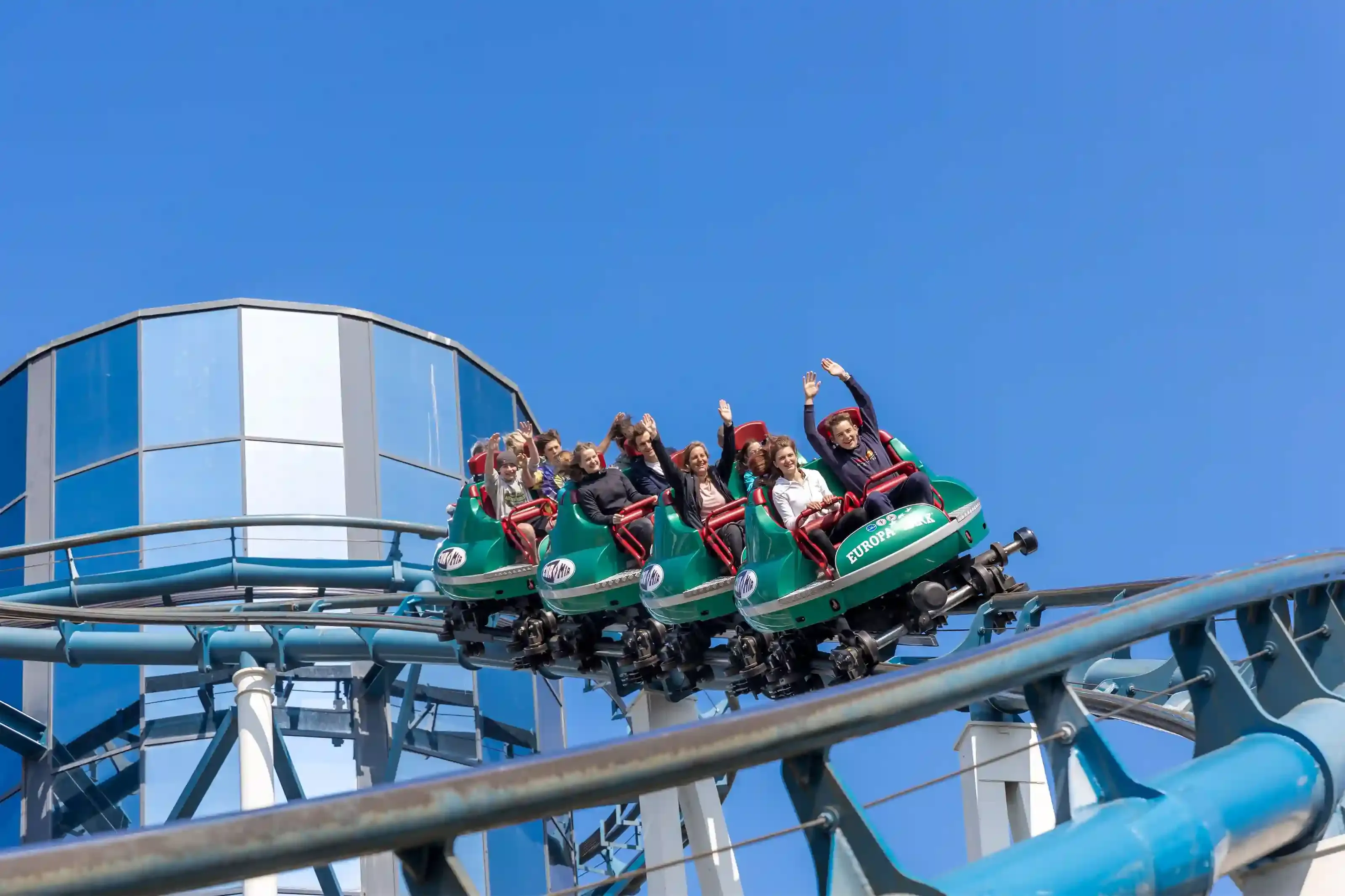 Riders on a steep rollercoaster drop at a thrill theme park near London on a clear day