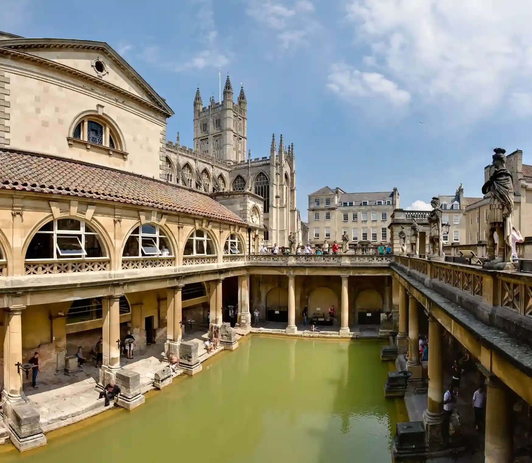 The steaming Great Bath at the Roman Baths in Bath with Bath Abbey behind, a popular day trip from London