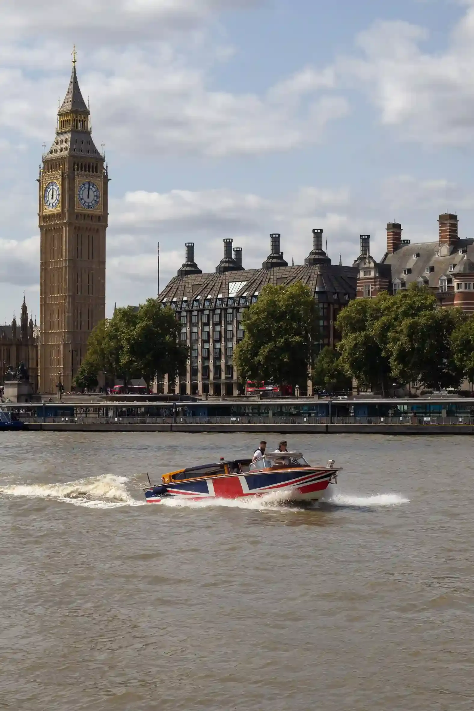 A self-drive electric picnic boat on the River Thames near Kingston upon Thames with passengers steering past riverside greenery