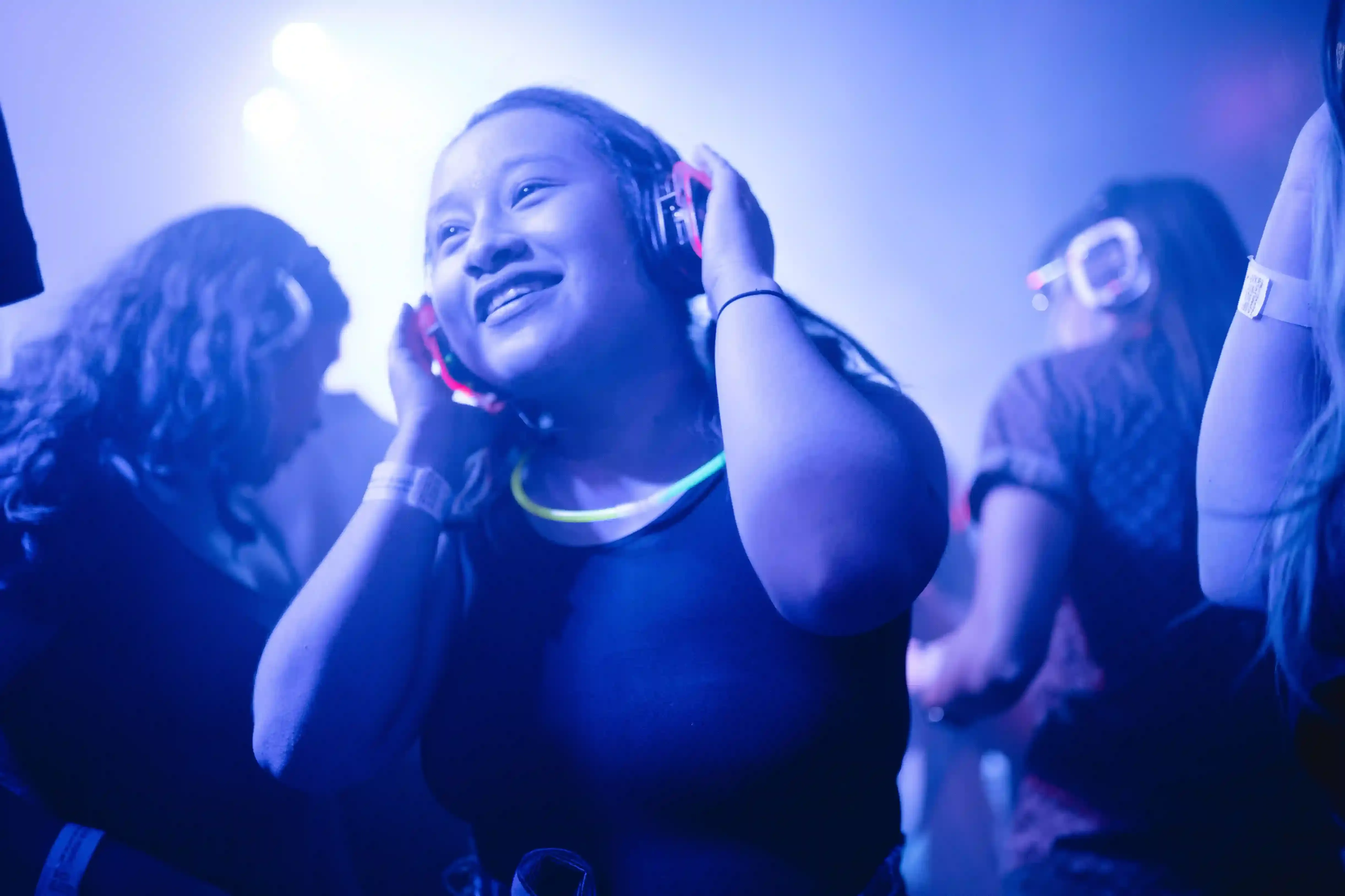A crowd dancing in glowing headphones at a silent disco boat party on the River Thames at night in London