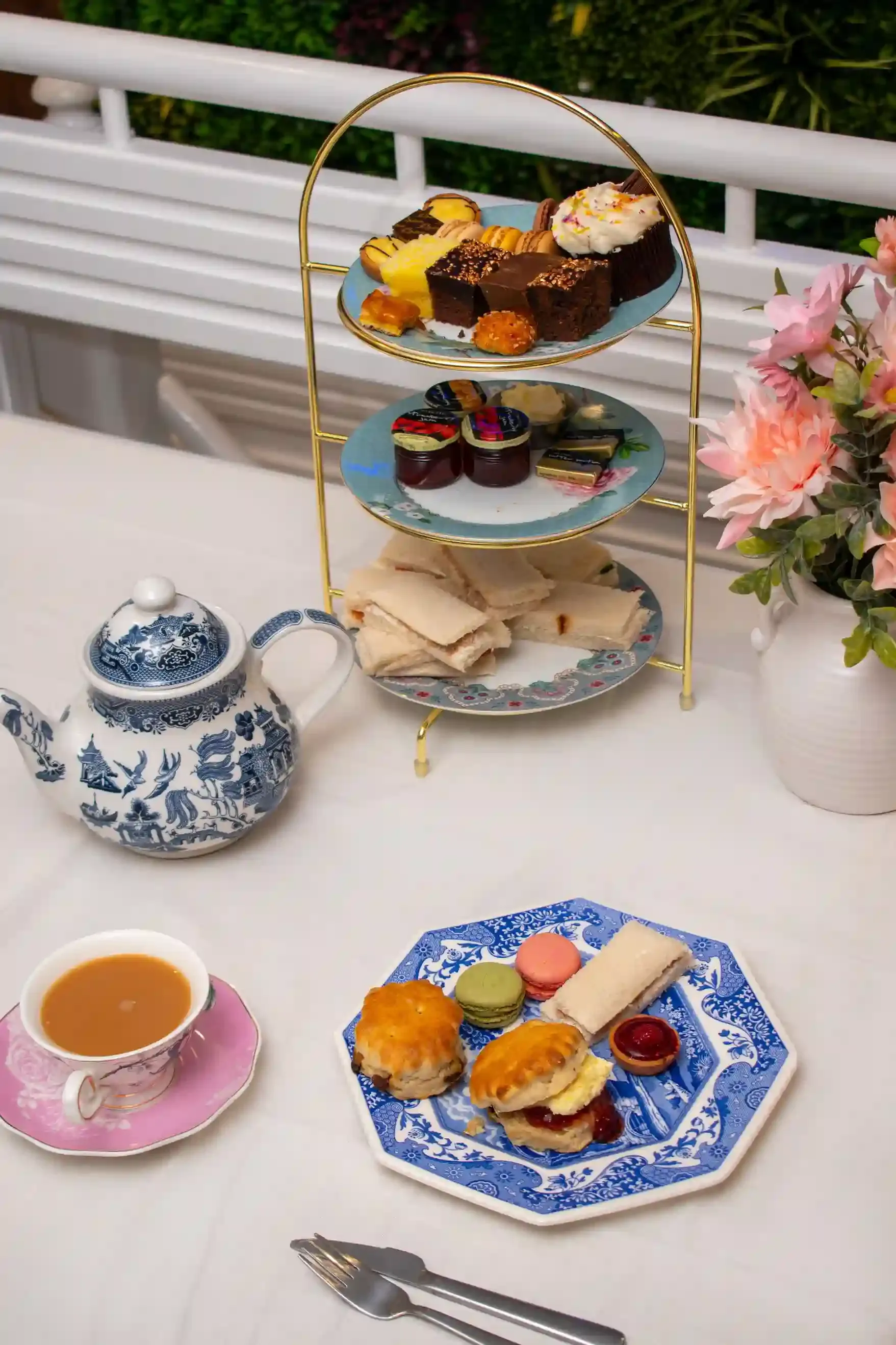 Tiered afternoon tea stand with cakes, scones and a teapot in an elegant grand London hotel room