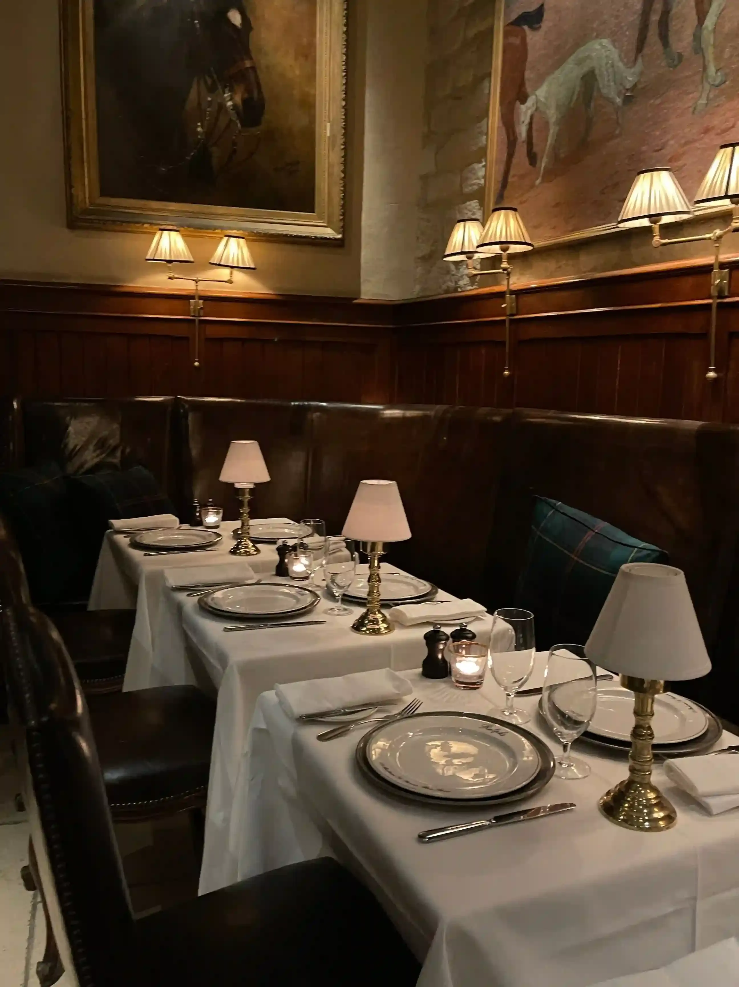 Wood-panelled dining room of a historic London restaurant with white-linen tables and framed cartoons on the walls